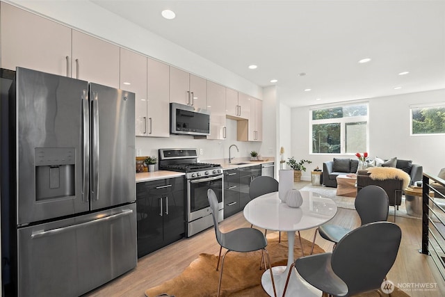 kitchen featuring stainless steel appliances, a sink, light wood-type flooring, light countertops, and recessed lighting