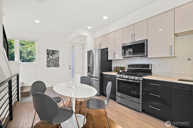 kitchen featuring appliances with stainless steel finishes, light wood-type flooring, light countertops, recessed lighting, and a sink