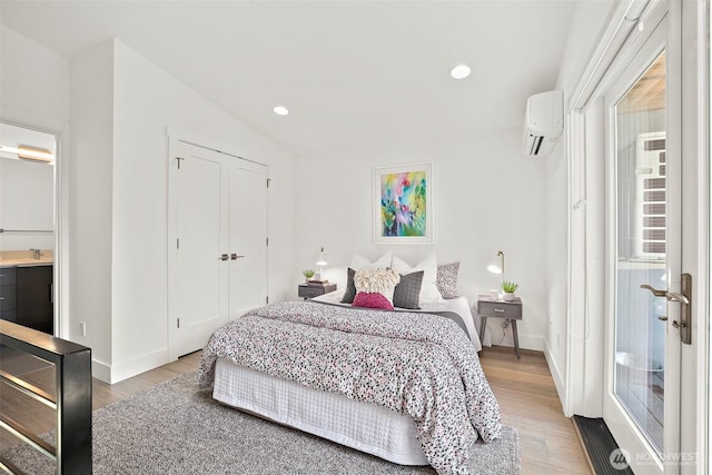 bedroom featuring an AC wall unit, light wood-style flooring, a sink, baseboards, and recessed lighting