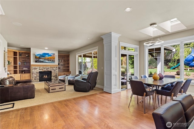 living area with a skylight, baseboards, a stone fireplace, light wood-style floors, and recessed lighting