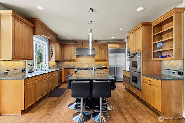 kitchen featuring a sink, dark stone counters, decorative backsplash, a kitchen island with sink, and appliances with stainless steel finishes