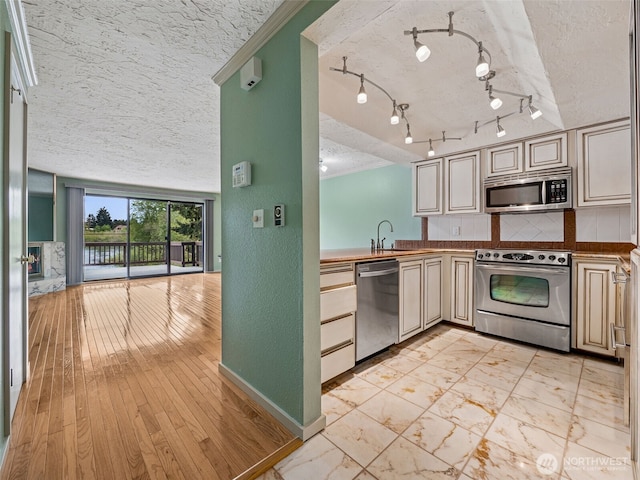 kitchen with appliances with stainless steel finishes, a textured ceiling, cream cabinets, a sink, and baseboards