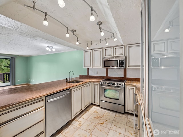 kitchen with appliances with stainless steel finishes, a sink, cream cabinetry, a textured ceiling, and backsplash
