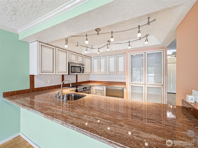 kitchen with appliances with stainless steel finishes, dark stone counters, a sink, a textured ceiling, and a textured wall