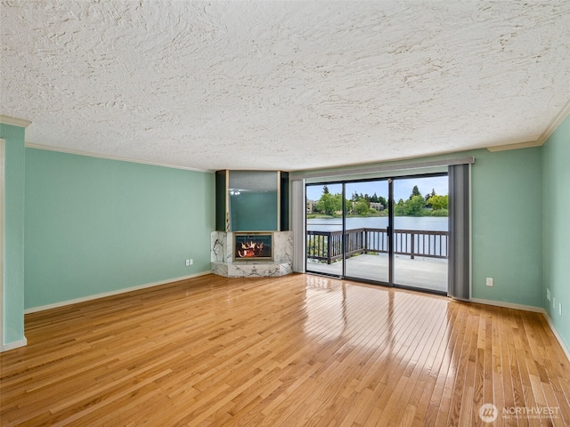 unfurnished living room featuring wood-type flooring, crown molding, a glass covered fireplace, a textured ceiling, and a water view
