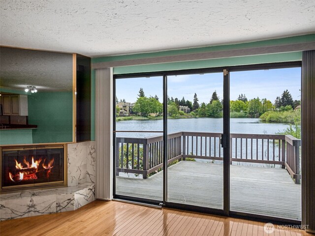 doorway to outside with a textured ceiling, a water view, wood finished floors, and a glass covered fireplace