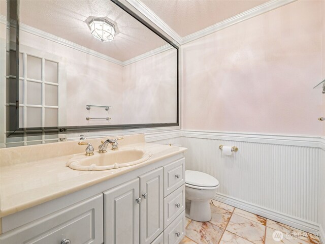 half bathroom with toilet, marble finish floors, ornamental molding, vanity, and wainscoting