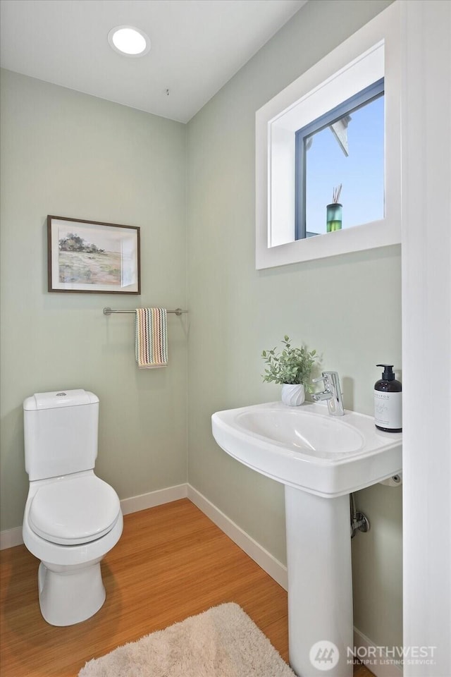 bathroom featuring baseboards, wood finished floors, toilet, and a sink