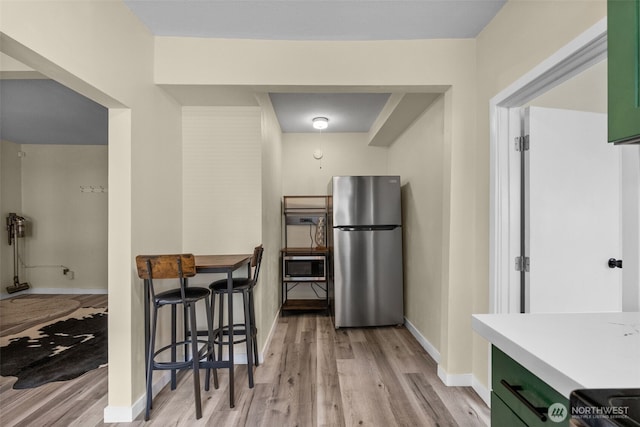 kitchen featuring stainless steel appliances, light wood finished floors, green cabinetry, baseboards, and light countertops