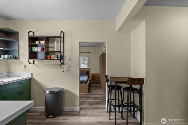 kitchen featuring green cabinets, wood finished floors, light countertops, and baseboards