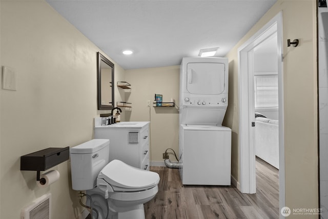 bathroom with stacked washer / drying machine, wood finished floors, toilet, baseboards, and vanity
