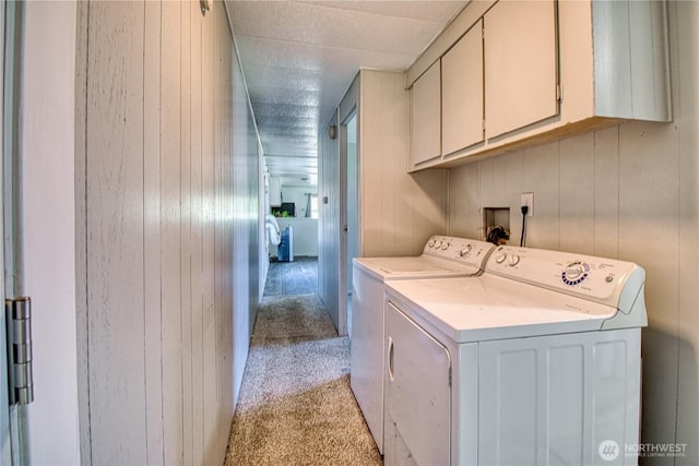laundry room with light carpet, washer and dryer, cabinet space, and wood walls