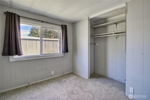 unfurnished bedroom featuring a closet, carpet, a textured ceiling, and wood walls