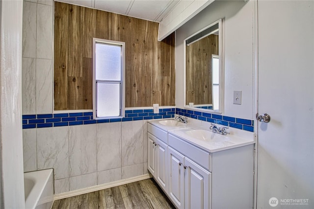 full bathroom featuring wood finished floors, tile walls, double vanity, and a tub to relax in