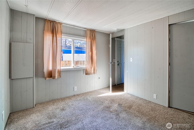 unfurnished room with carpet, wooden walls, and a textured ceiling