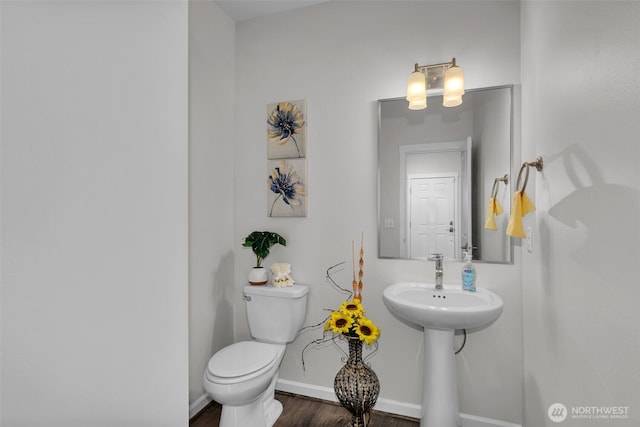 half bathroom with toilet, wood finished floors, baseboards, and a sink