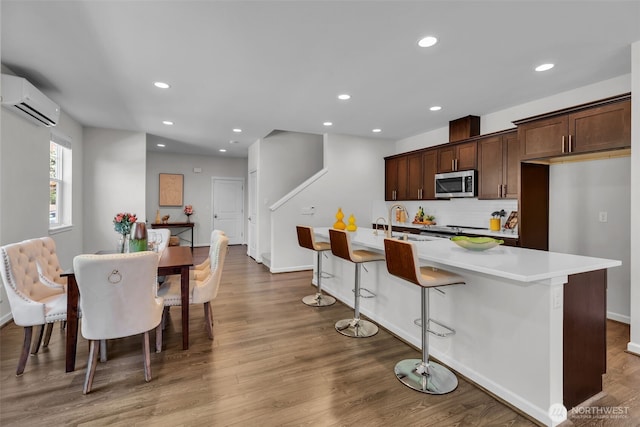 kitchen with stainless steel microwave, an AC wall unit, tasteful backsplash, wood finished floors, and recessed lighting
