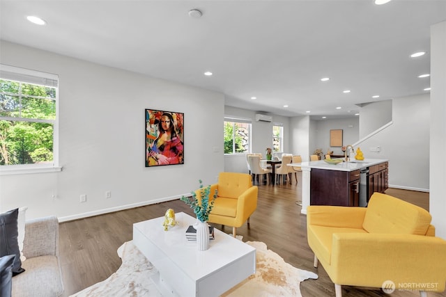 living room with recessed lighting, wood finished floors, a wall mounted AC, and baseboards