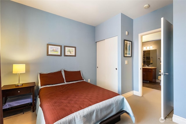 bedroom with a closet, carpet floors, ensuite bath, and baseboards