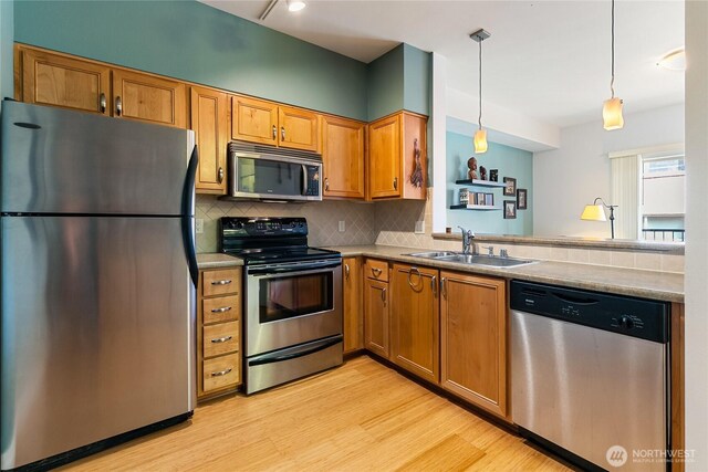 kitchen featuring stainless steel appliances, a sink, light wood finished floors, backsplash, and brown cabinets