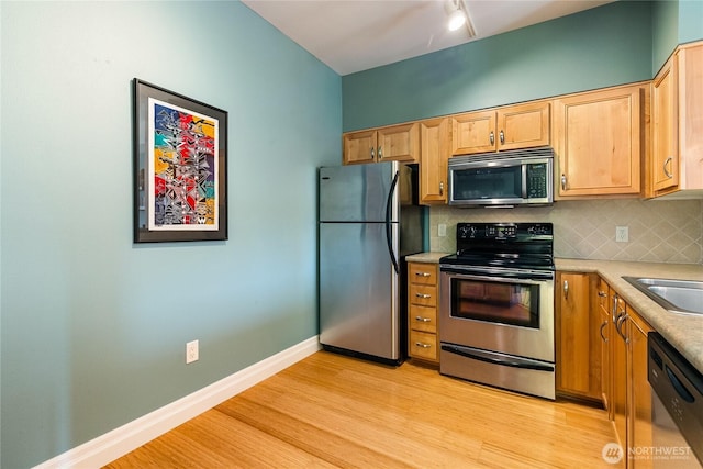kitchen featuring stainless steel appliances, light wood-style flooring, decorative backsplash, light countertops, and baseboards