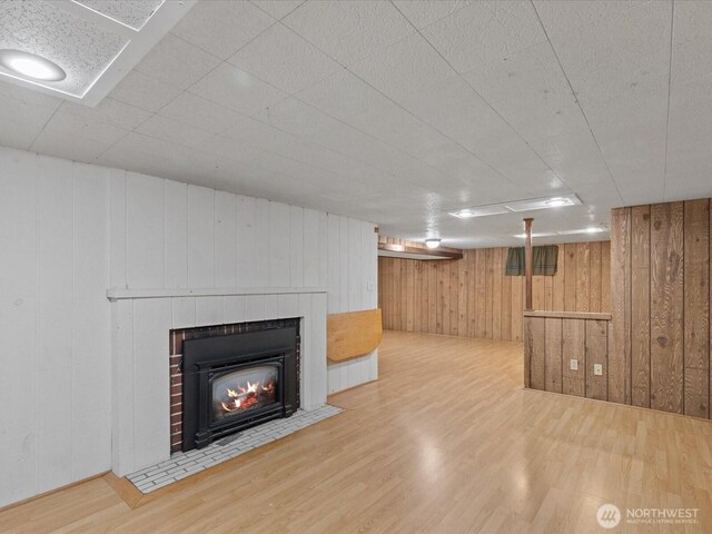 finished basement with wood finished floors, wood walls, and a fireplace with flush hearth