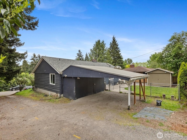 view of side of property featuring a carport, fence, roof with shingles, and dirt driveway