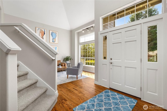 foyer entrance featuring wood finished floors, stairway, and high vaulted ceiling