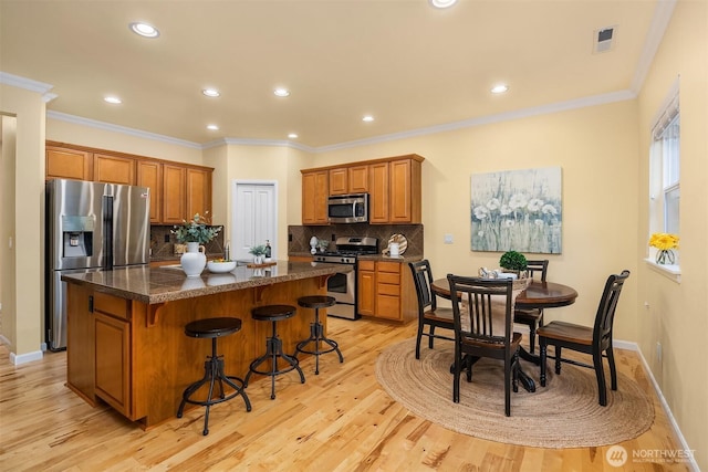 kitchen featuring stainless steel appliances, a center island, decorative backsplash, light wood-type flooring, and a breakfast bar