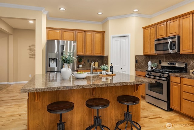 kitchen with stainless steel appliances, a kitchen bar, light wood finished floors, brown cabinetry, and recessed lighting