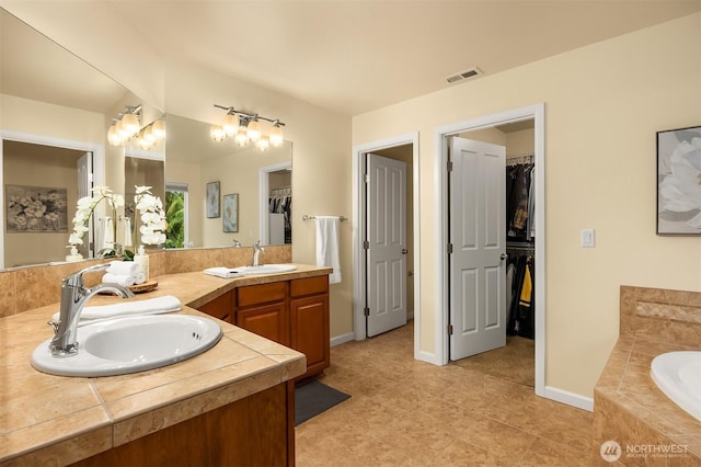 full bath featuring a spacious closet, a garden tub, double vanity, baseboards, and tile patterned flooring