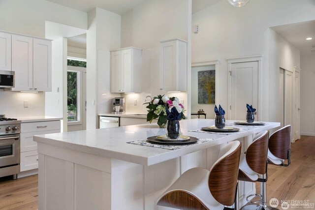 39195 Blackmouth Pl NE, Hansville, WA 98340 - kitchen with gas range, light wood-type flooring, white cabinetry, and a towering ceiling