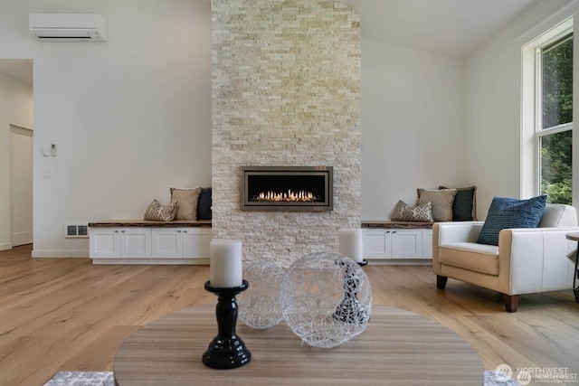 39195 Blackmouth Pl NE, Hansville, WA 98340 - living area with an AC wall unit, lofted ceiling, light wood-style floors, a stone fireplace, and baseboards