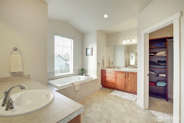 full bath with two vanities, a bath, and vaulted ceiling