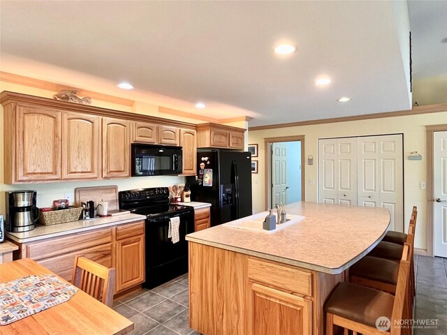 kitchen with black appliances, a sink, light countertops, a breakfast bar, and a center island with sink