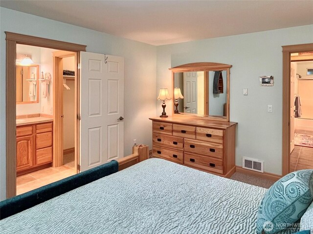 bedroom featuring light colored carpet, a walk in closet, connected bathroom, and baseboards