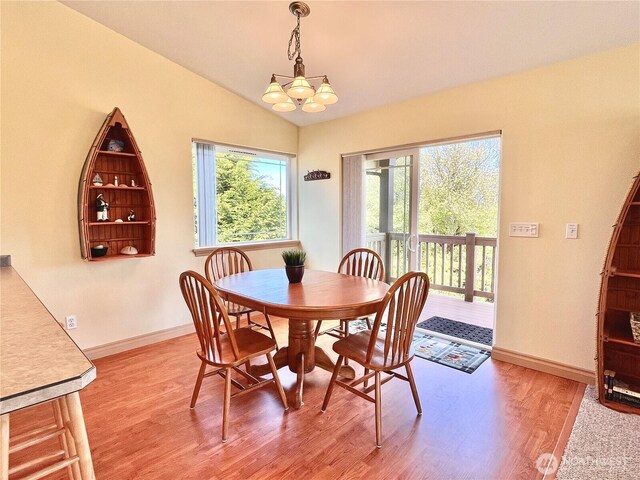 dining space with a chandelier, light wood-style flooring, baseboards, and lofted ceiling