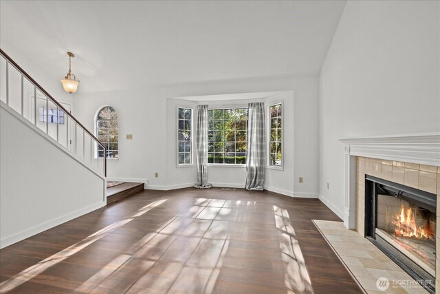 unfurnished living room with a tile fireplace, stairway, wood finished floors, and baseboards