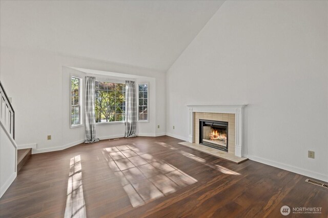 unfurnished living room featuring wood finished floors, a tile fireplace, high vaulted ceiling, and baseboards