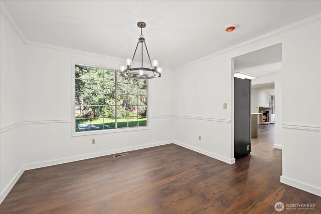unfurnished dining area with a chandelier, crown molding, dark wood finished floors, a lit fireplace, and baseboards