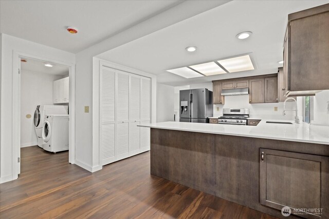 kitchen with stainless steel appliances, a sink, separate washer and dryer, light countertops, and dark wood finished floors