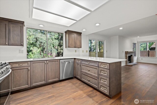 kitchen featuring stainless steel appliances, a peninsula, a sink, dark wood-style flooring, and recessed lighting