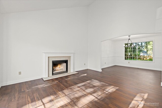 unfurnished living room featuring high vaulted ceiling, a chandelier, a tile fireplace, dark wood-type flooring, and baseboards