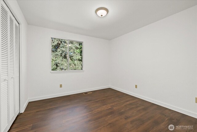 unfurnished bedroom featuring baseboards, dark wood-style floors, and a closet