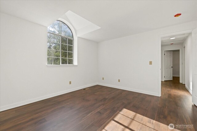 empty room featuring wood finished floors, baseboards, and lofted ceiling