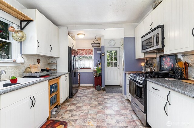 kitchen with appliances with stainless steel finishes, backsplash, white cabinetry, and baseboards