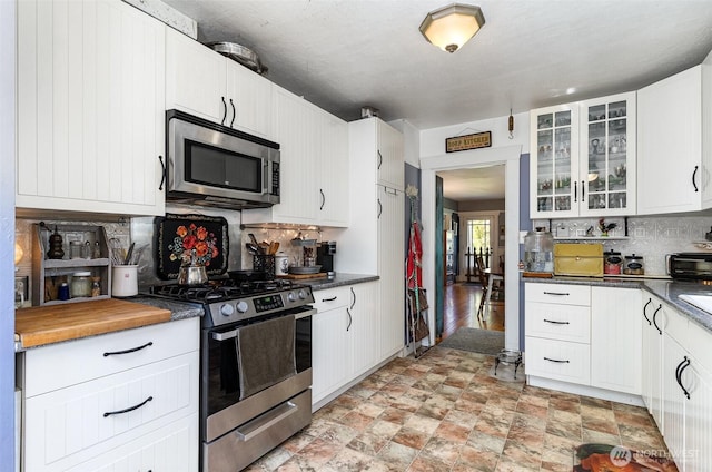 kitchen with stainless steel appliances, decorative backsplash, glass insert cabinets, stone finish floors, and white cabinets