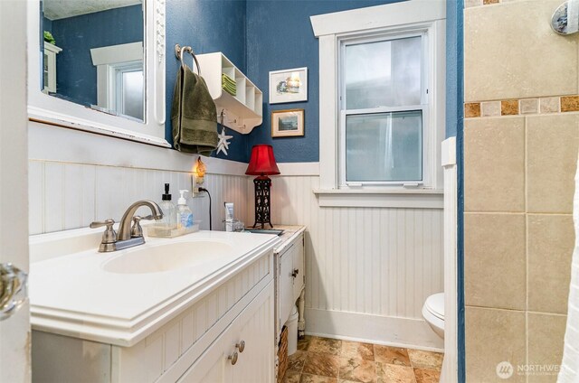 bathroom with wainscoting, toilet, vanity, and baseboards