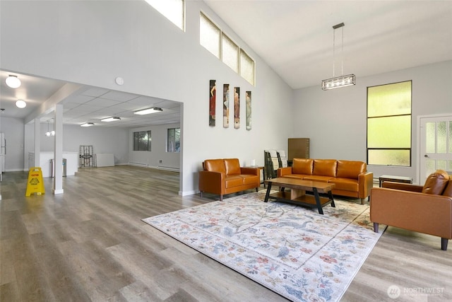 living area featuring healthy amount of natural light, wood finished floors, baseboards, and a high ceiling