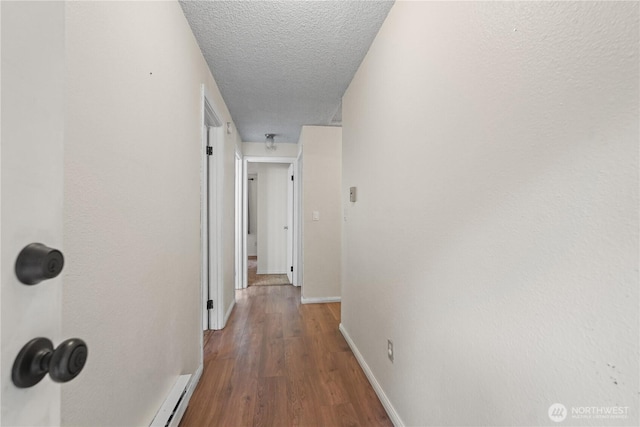 corridor with wood finished floors, a textured ceiling, and baseboards